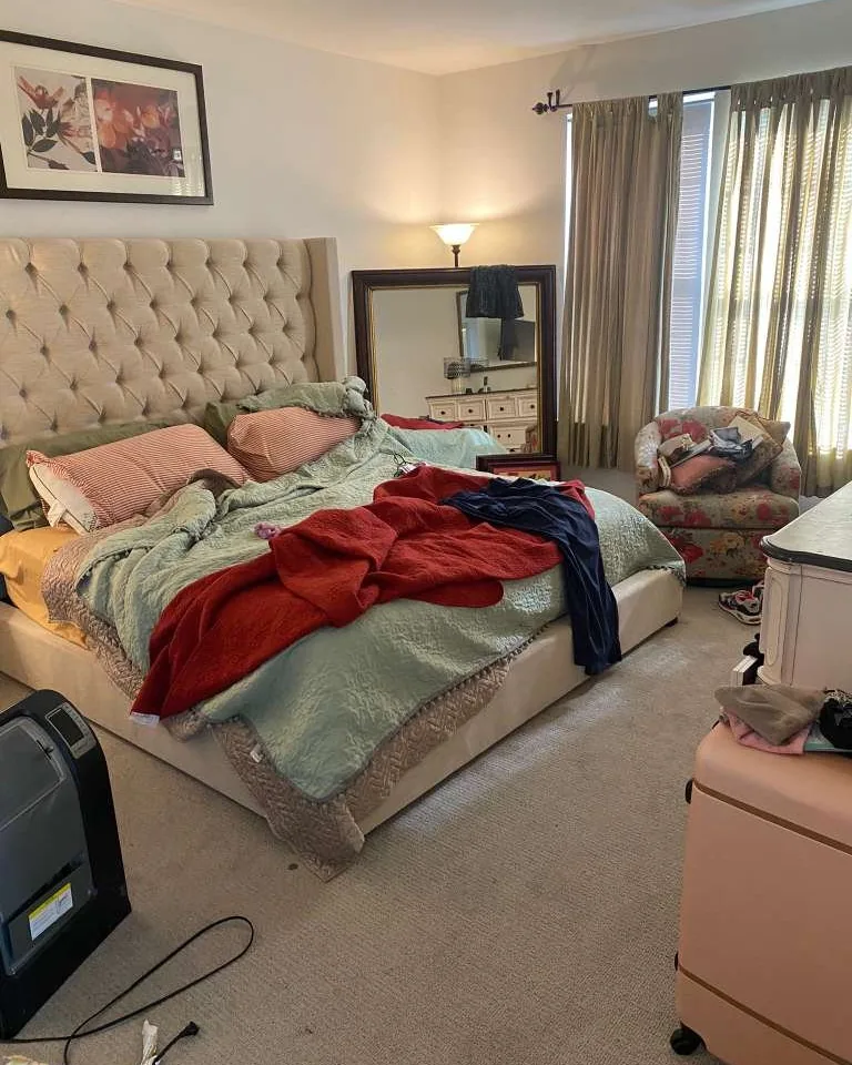 A bedroom with the bed unmade and clothes across it.