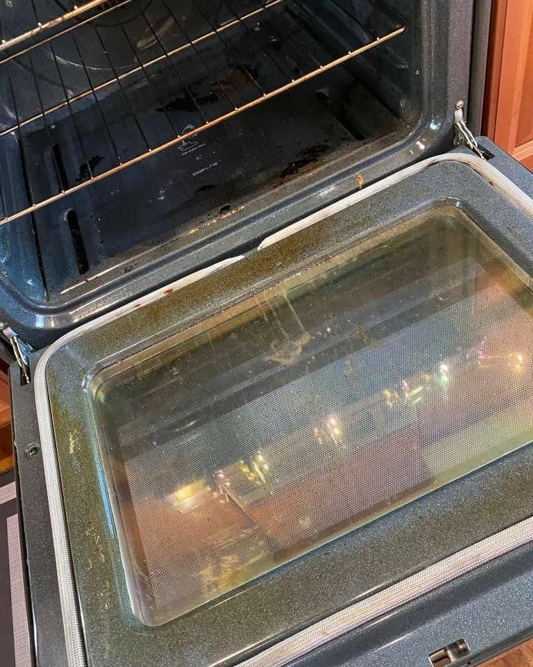 An oven door glass darkened by baked on residue.