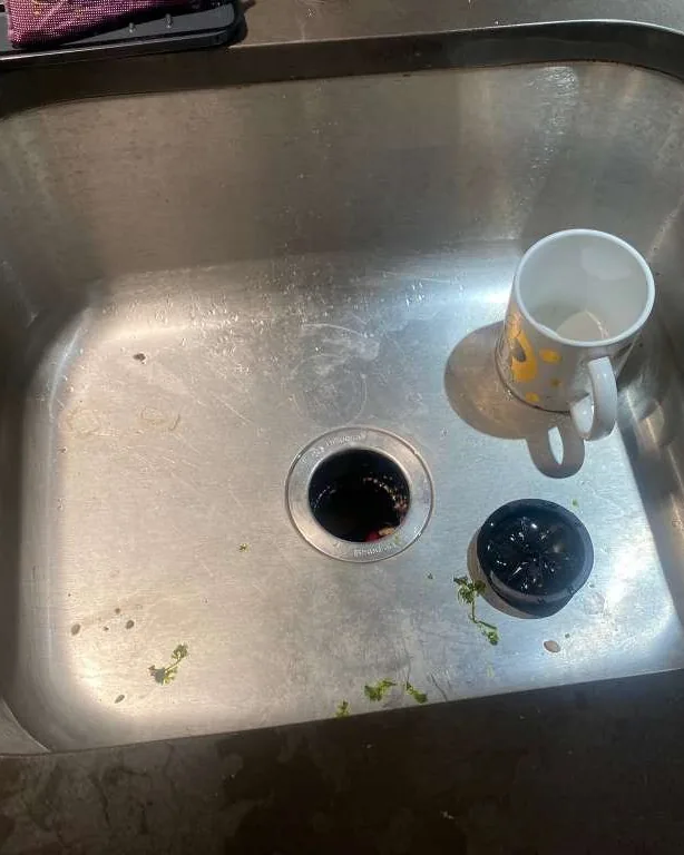 A stainless kitchen sink with dishes and food waste in the drain.