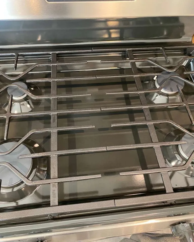 A stainless gas range, cleaned, with the burner grates back in place.