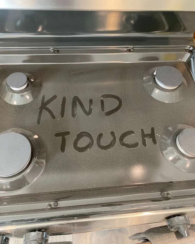 The same gas range before cleaning, with the words Kind Touch written by a finger through the grease.