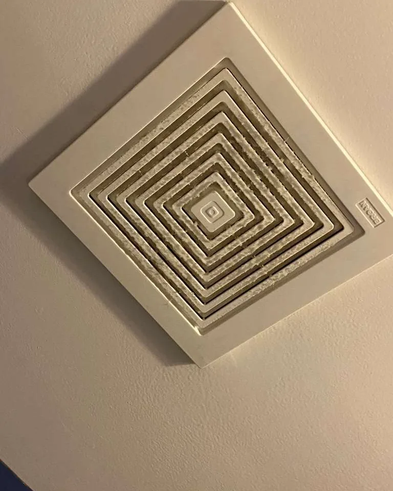 A ceiling exhaust vent grey with dust.